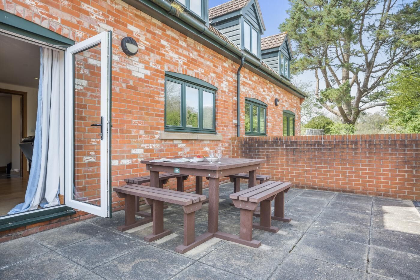 A brick house with a patio table and benches, a sliding glass door, and a brick wall.