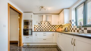 Een moderne keuken met witte kasten, een roestvrijstalen afzuigkap, een zwart-wit geruit achterwand en een raam met jaloezieën.