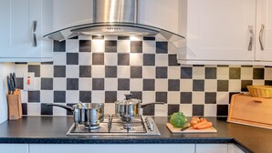Een moderne keuken met een gasfornuis, roestvrijstalen pannen en een geruit spatwand.