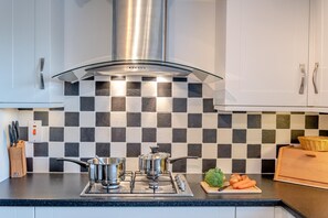 A modern kitchen with a gas stove, stainless steel pots, and a checkered backsplash. - 2 Bed in Bridport (oc-regis) (Charmouth)