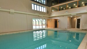 En indendørs swimmingpool med klart vand, flisegulv og et hvælvet loft med vinduer.