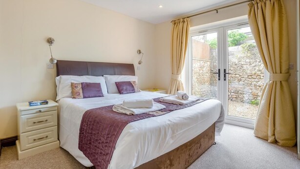 A bedroom with a bed, bedside tables, a nightstand, and a window with curtains. - 2 Bed in Bridport (oc-restw) (Charmouth)