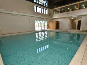 Ein Innenpool mit klarem, blauem Wasser, Fliesenboden und einer hohen Decke mit Fenstern.