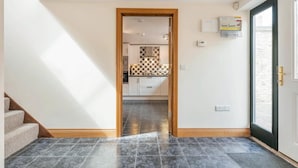 A hallway leading to a kitchen with a checkered backsplash, a door with a handle, and a thermostat on the wall. - 3 Bed in Bridport (oc-tcsaila) (Charmouth)