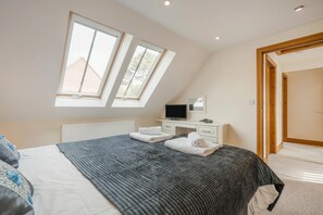 Ein Schlafzimmer mit Bett, Schreibtisch, Fernseher und zwei Oberlichtern.