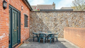 A brick building with a stone wall, a green door, and a table with chairs in the courtyard. - 3 Bed in Bridport (oc-tcsaila) (Charmouth)