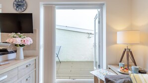 Ett rum med en tv, en vas med blommor, ett bord med en lampa och utsikt över en balkong.
