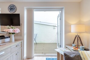 Ein Zimmer mit Fernseher, Blumen in einer Vase, einem Tisch mit Lampe und Blick auf einen Balkon.