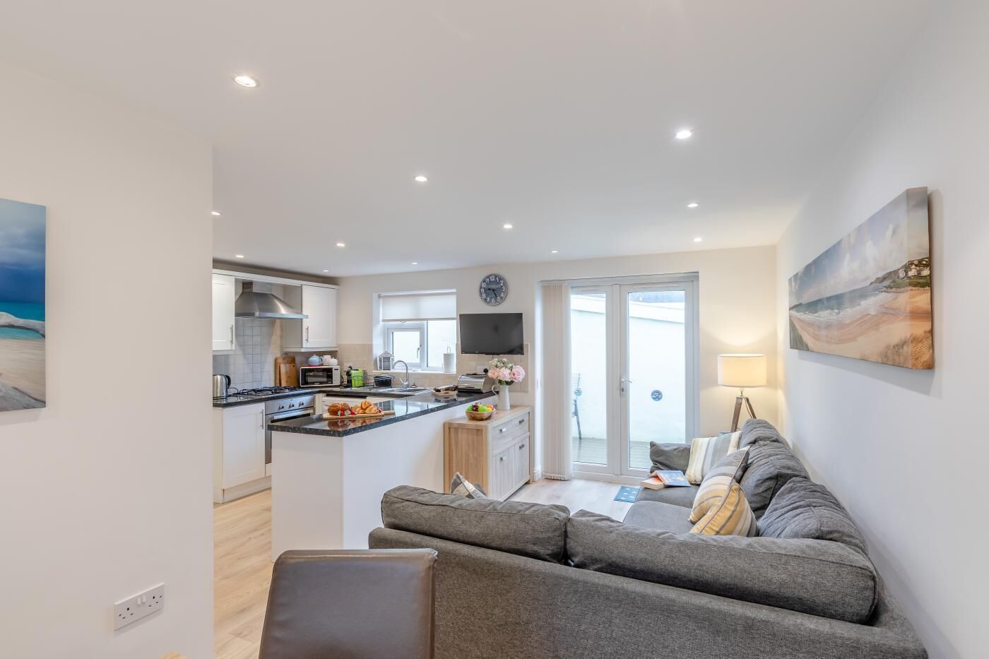 Et moderne køkken med en central ø, et spiseområde med en sofa og udsigt gennem en glasdør.
