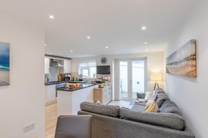 Eine moderne Küche mit einer zentralen Kochinsel, einem Essbereich mit einer Couch und Blick durch eine Glastür.