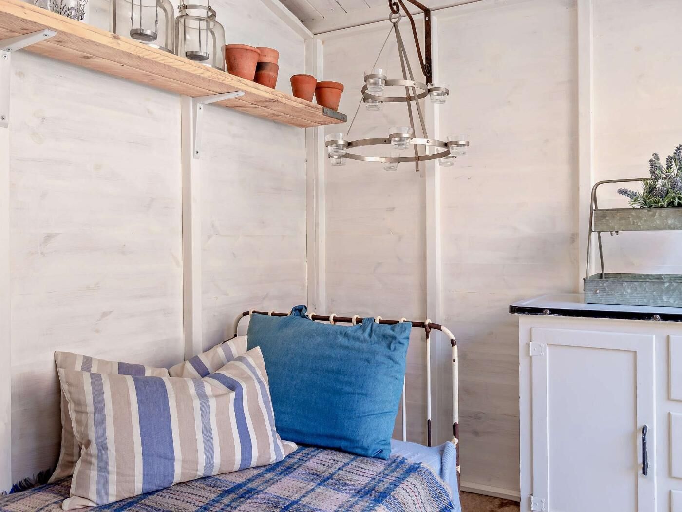 Una stanza con un letto, un armadio bianco, una lampada a sospensione e uno scaffale con piante in vaso.