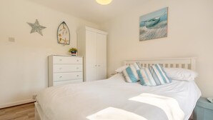 Une chambre à coucher comprenant un lit, une commode, une table de chevet, une décoration en forme d’étoile de mer et un tableau représentant un bateau.