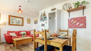 Un coin repas avec une table en bois dressée pour deux personnes, un canapé rouge et un miroir au mur.
