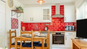 Une cuisine avec des meubles blancs, un pare-feu rouge, un four encastré et un four à micro-ondes.