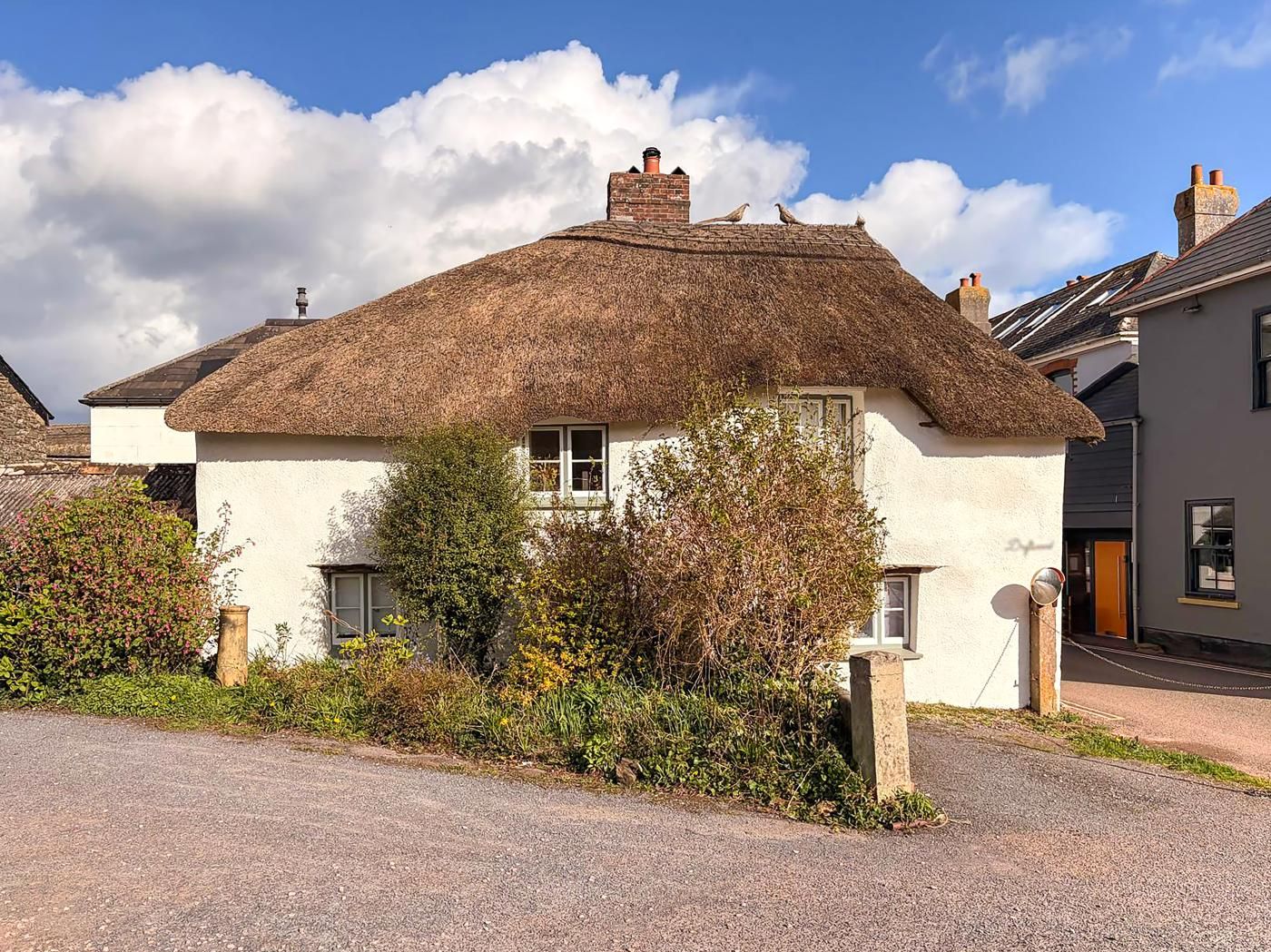 A traditional thatched-roof house with a white exterior, surrounded by greenery and a gravel driveway.