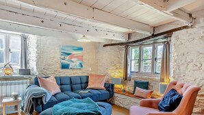 A cozy room with a blue sofa, a pink armchair, a wooden floor, and a stone wall. - 2 Bed in Kingsbridge (oc-94125) (Malborough)