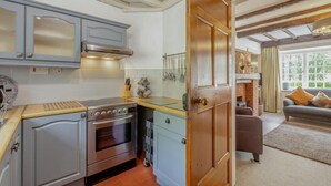 A kitchen with a stove, oven, and cabinets, leading to a living area with a sofa and a fireplace. - 3 Bed in Ambleside (oc-96511) (Claife)