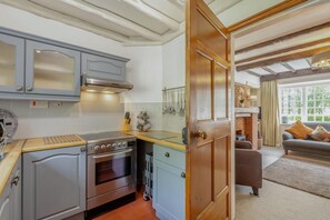 A kitchen with a stove, oven, and cabinets, leading to a living area with a sofa and a fireplace. - 3 Bed in Ambleside (oc-96511) (Claife)