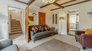A living room with a sofa, a brown leather chair, a round mirror, a tall floor lamp, and a staircase leading to another room. - 3 Bed in Ambleside (oc-96511) (Claife)