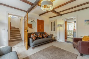 A living room with a sofa, a brown leather chair, a round mirror, a tall floor lamp, and a staircase leading to another room. - 3 Bed in Ambleside (oc-96511) (Claife)