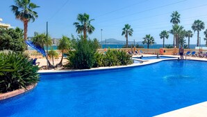 Une piscine bordée de palmiers, avec des chaises longues et une vue sur la mer.
