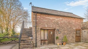 A stone building with a wooden door, a small staircase, and a weather vane. - 1 Bed in Usk- (oc-79936) (Kingcoed)