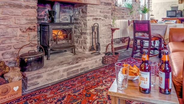 A rustic stone fireplace with a wood-burning stove, a dining area with a table set for two, and a cozy seating arrangement. - 1 Bed in Usk- (oc-79936) (Kingcoed)