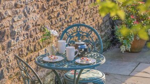 A stone wall, a round table with a teapot, two cups, and a vase with flowers. - 1 Bed in Usk- (oc-79936) (Kingcoed)