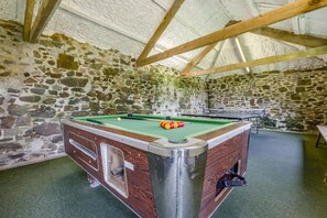 Ein Billardtisch mit Holzrahmen und grüner Spielbahn, umgeben von Steinwänden und einer Holzbalkendecke.