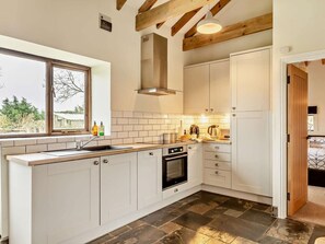 Cuina moderna amb armaris blancs, forn integrat i finestra amb vista a vegetació.