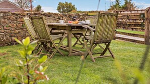 A stone wall, a wooden table with chairs, and a grassy area. - 2 Bed in Bude (oc-04727) (Poundstock)