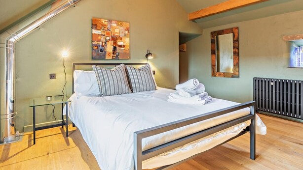 Un dormitorio con cama, una mesita de vidrio, un radiador y un tragaluz.