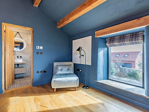 Ein Zimmer mit Holzboden, blauer Wand, Fenster mit Ausblick, einem Bett, einem Nachttisch und einer Lampe.