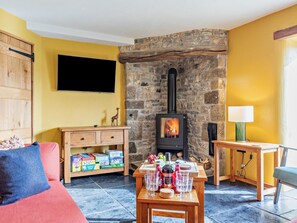 Ein gemütliches Wohnzimmer mit Kamin aus Stein, einem Flachbildfernseher, einer Holzeinrichtung mit Gesellschaftsspielen und einem Tisch mit Gläsern und Flaschen.