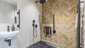 Un baño moderno con un lavamanos blanco, un espejo, una ducha con cabezal de ducha negro de mano y pared con patrón de espiga.