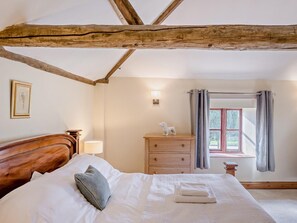 A bedroom with a wooden ceiling, a bed with white linens, a nightstand with a lamp, a dresser, and a window with curtains. - 2 Bed in Thetford (oc-57886) (Saham Toney)