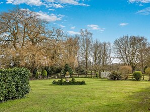 A well-maintained garden with a variety of trees, a neatly trimmed lawn, and a decorative stone feature. - 2 Bed in Thetford (oc-57886) (Saham Toney)