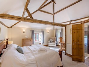 A bedroom with a large bed, wooden beams on the ceiling, a dresser, a chair, and a door leading to another room. - 2 Bed in Thetford (oc-57886) (Saham Toney)