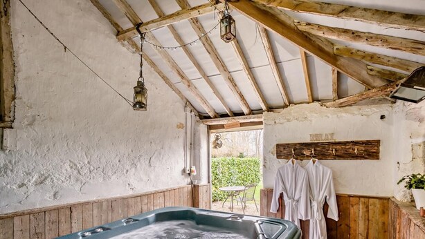 Ein rustikaler Wellnessbereich mit Whirlpool, Holzwänden und aufgehängten Bademänteln.
