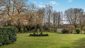 Ein gepflegter Garten mit verschiedenen Bäumen, einem ordentlich geschnittenen Rasen und einer Steinfontäne.