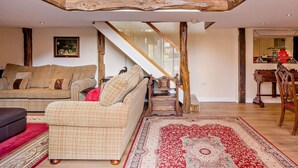 Een ruime woonruimte met een hoge plafond, een trap en een eethoek met een houten tafel en stoelen.