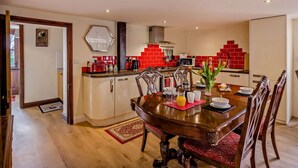 Een eethoek met een houten tafel en stoelen, een keuken met een rode betegelde achterwand, en een klok aan de muur.