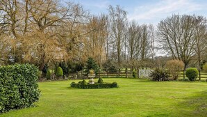 Een goed onderhouden tuin met verschillende bomen, een strak gemaaid gazon en een rond bloembed in het midden.