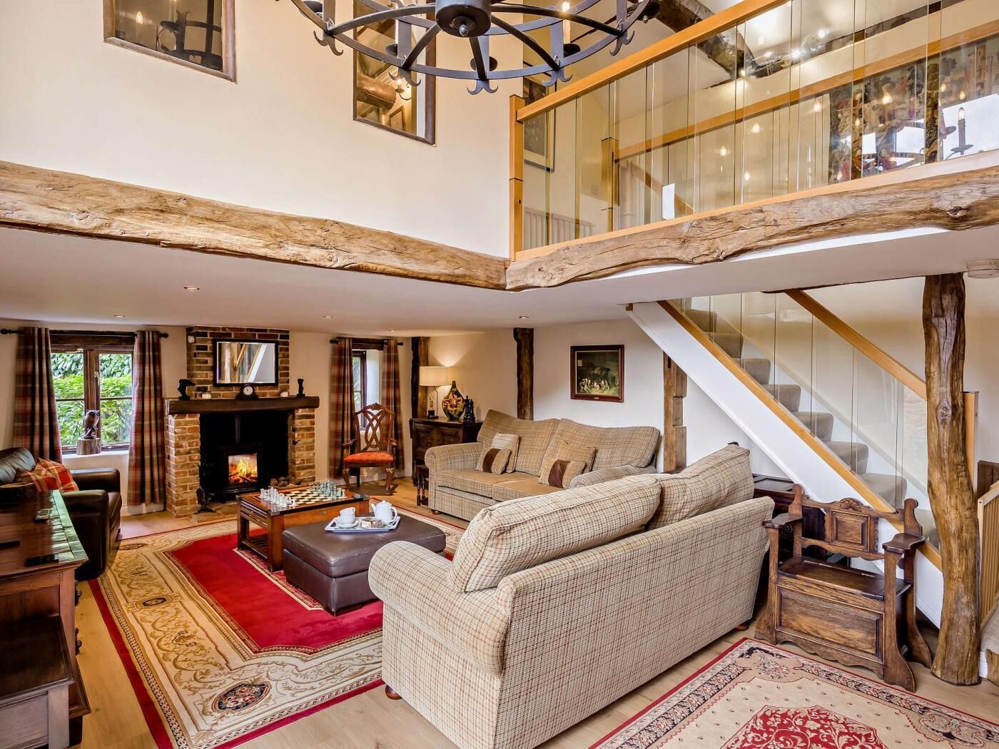 A spacious living area with a fireplace, a sofa set, a wooden staircase, and a high ceiling with exposed beams.