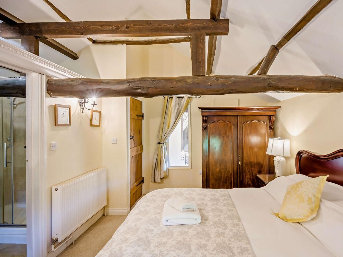 Een slaapkamer met een houten plafond, een bed met een geel-wit kussen, een houten kledingkast en een radiator.