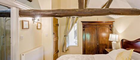 Een slaapkamer met een houten plafond, een bed met een geel-wit kussen, een houten kledingkast en een radiator.