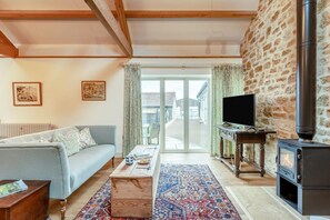 Ein Wohnzimmer mit einer Couch, einem Couchtisch, einem Fernseher, einem Kamin und Blick durch eine Glastür.