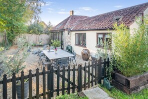 Eine Terrasse mit Tisch und Stühlen, ein Holzzaun und ein Haus mit einem Ziegeldach.