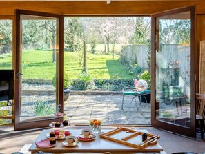 Ein Zimmer mit einer großen Glastür, die auf eine Terrassenanlage nach außen führt. Im Inneren steht ein Tisch, gedeckt mit Teetassen, Untertassen und einer Platte mit einem Teekessel.