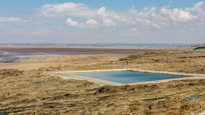Un paisatge rocosós amb piscina i platja a la distància.